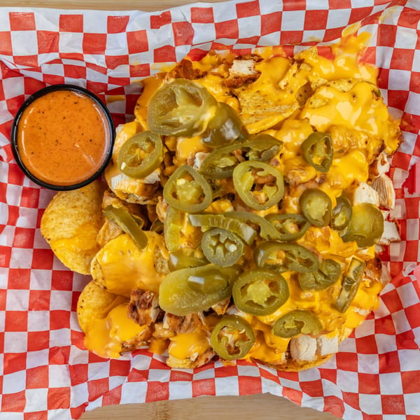 Kluckin' Chicken nachos with melted cheese, jalapenos, fried chicken pieces, and a side of sauce.