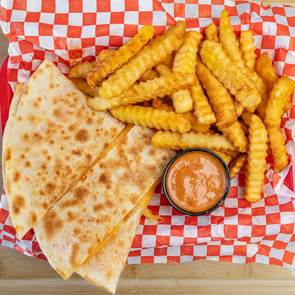 Quesadilla slices, crinkle-cut fries, and a dipping sauce in a red and white checkered basket.