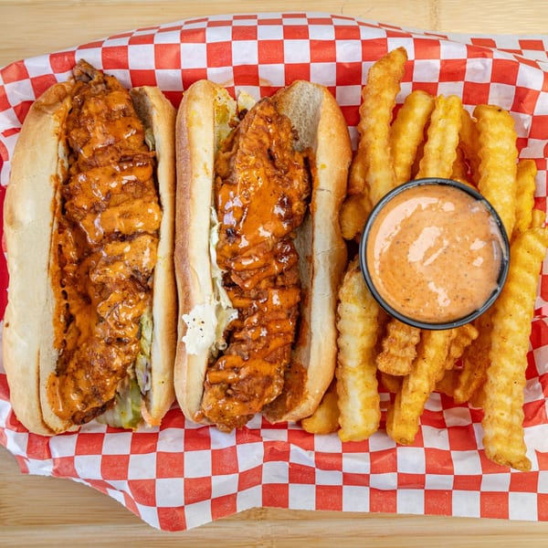 Two fried chicken sandwiches with sauce and fries with dipping sauce in a red and white basket.
