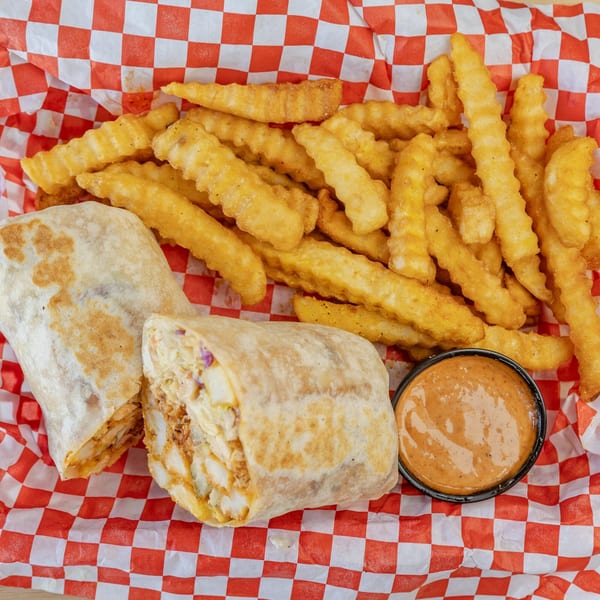 A fried chicken burrito, crinkle-cut fries, and dipping sauce in a red and white checkered basket.