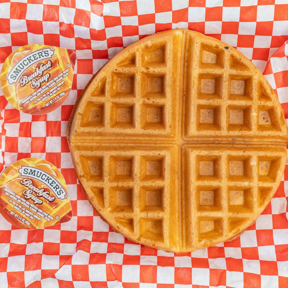 A golden waffle and two Smucker's syrup cups on red and white checkered paper.