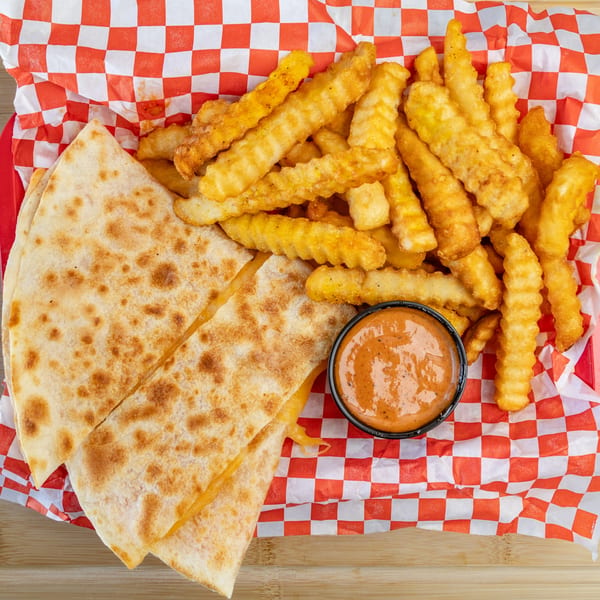 Quesadilla slices, crinkle-cut fries, and a dipping sauce in a red and white checkered basket.