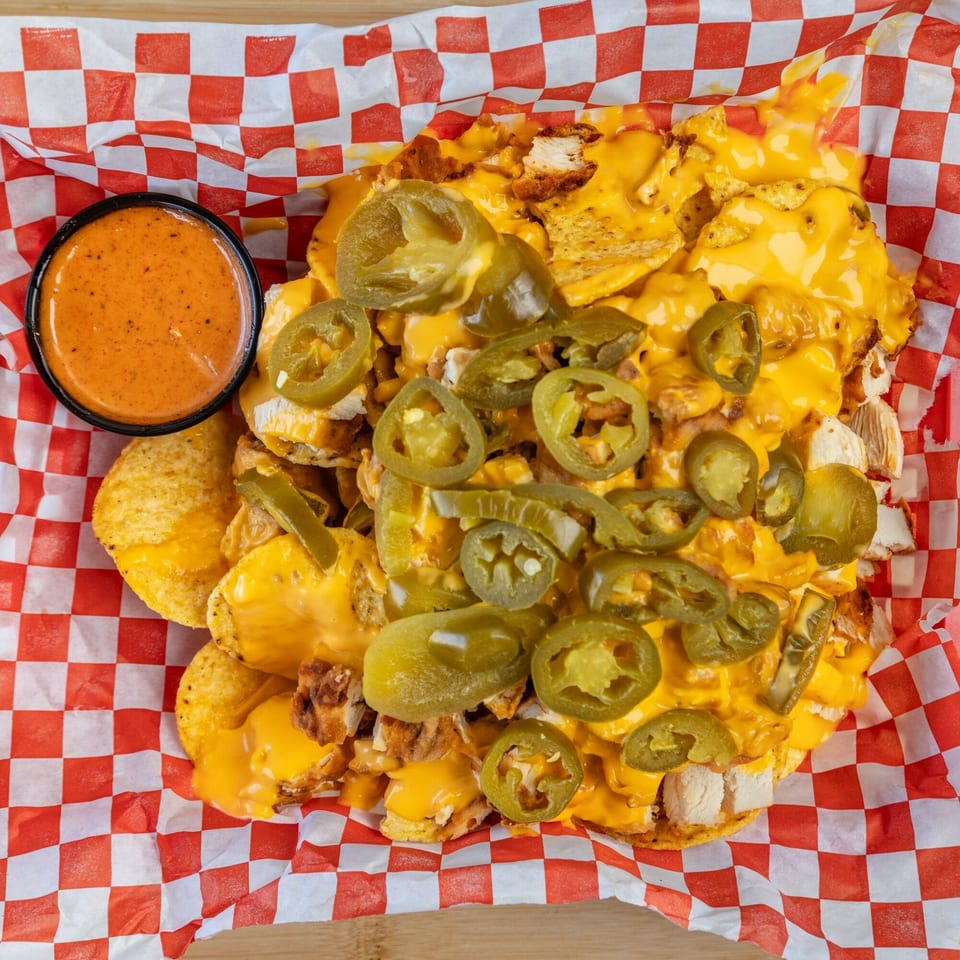 Kluckin' Chicken nachos with melted cheese, jalapenos, and a side of dipping sauce.