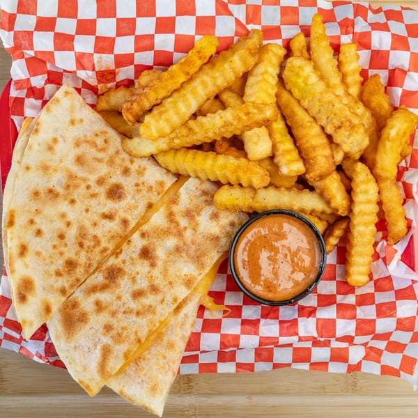 Quesadilla slices, crinkle-cut fries, and a dipping sauce in a red and white checkered basket.