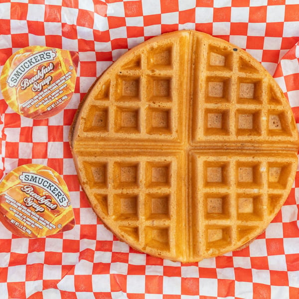 A golden waffle and two Smucker's syrup cups on red and white checkered paper.